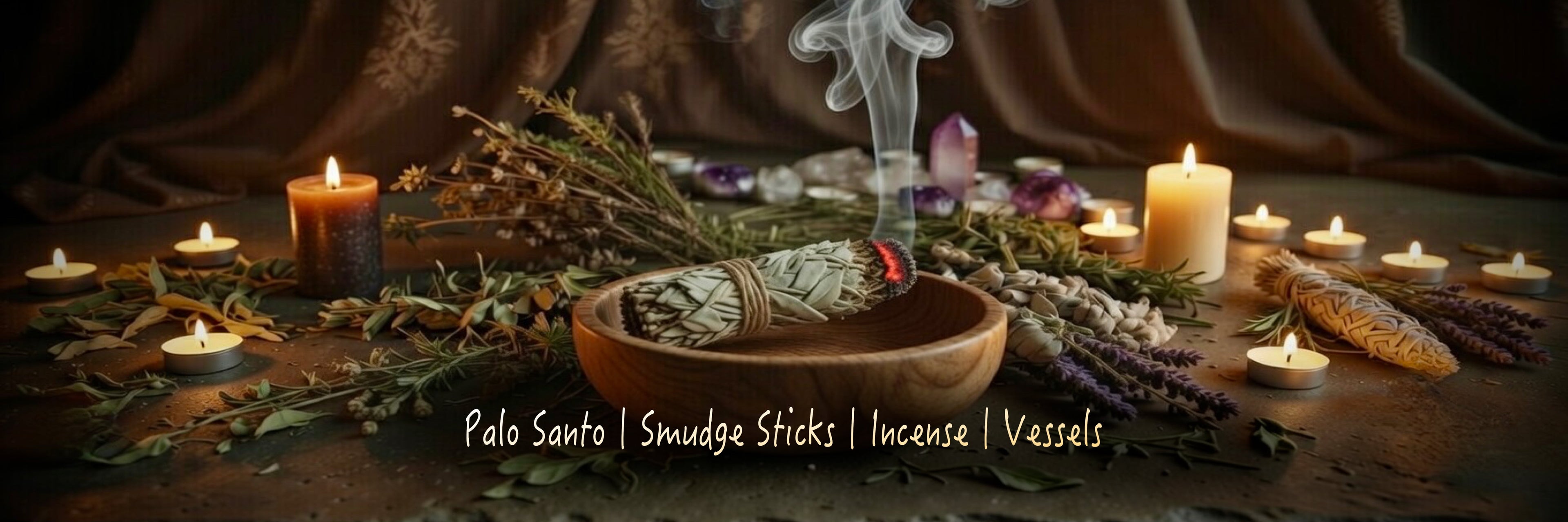Wooden bowl containing a lit sage smudge stick, surrounded by herbs and lit candles on a dark background