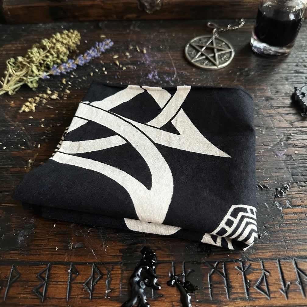 Black folded altar cloth with white design on a wooden surface with occult items.