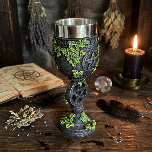 Decorative resin chalice with pentacle design on a wooden surface with candles and herbs.
