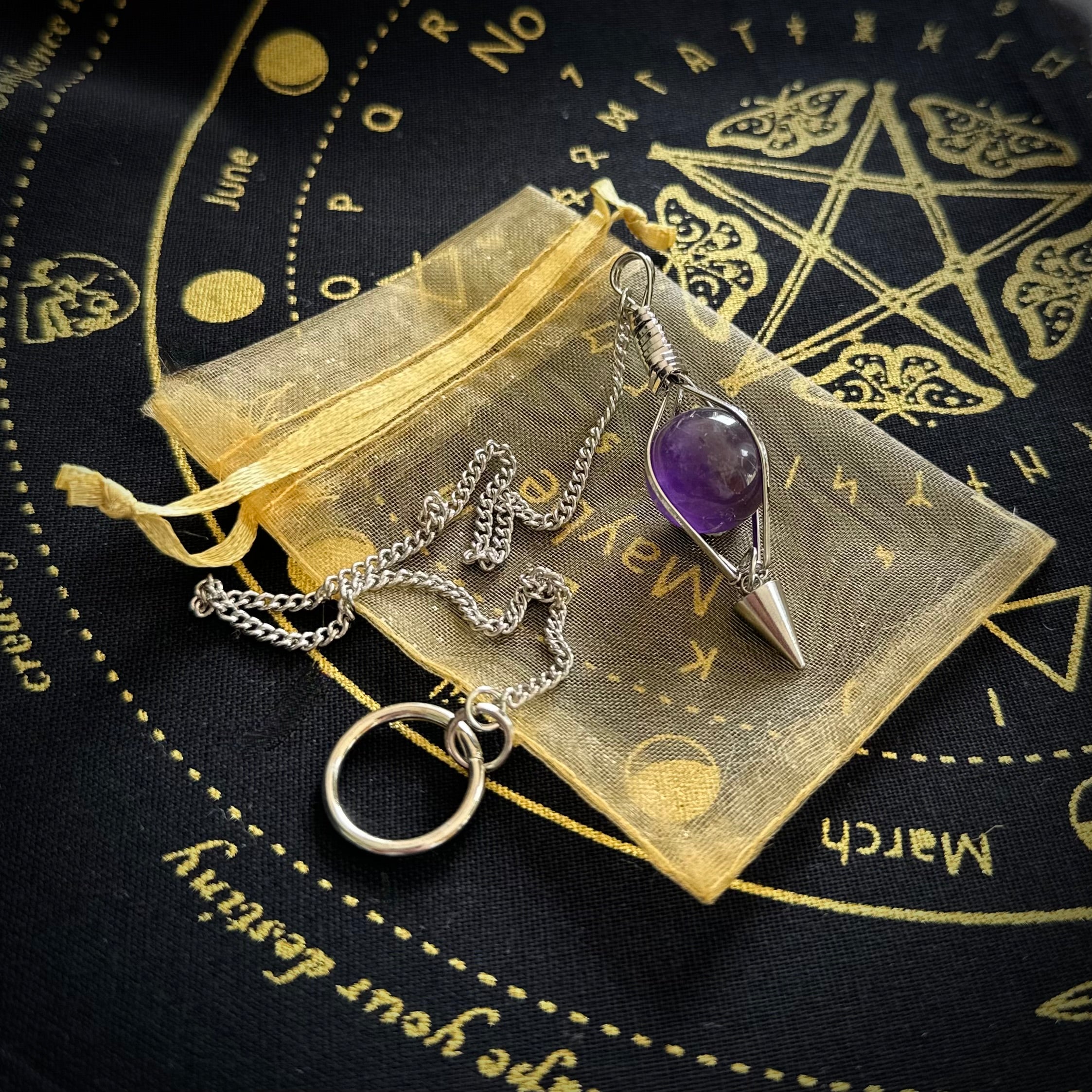 Amethyst pendulum on a gold drawstring bag with mystic moth design cloth background