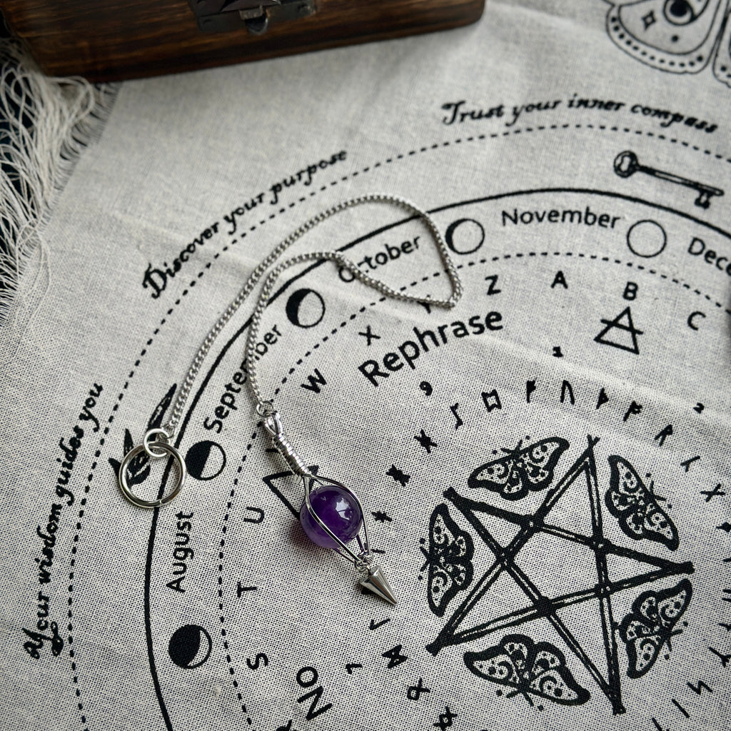 Silver tone pendulum featuring a caged amethyst on a divination cloth