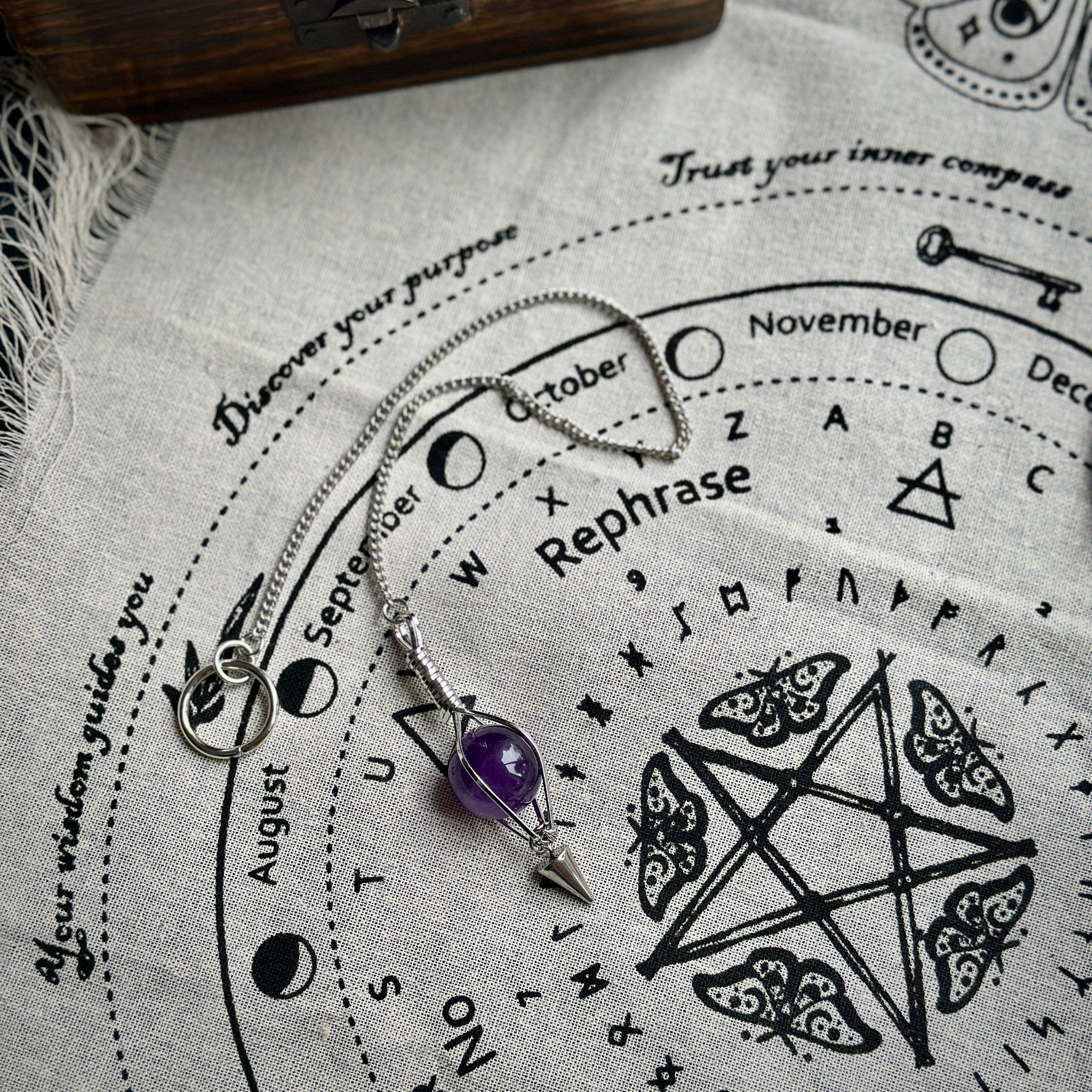 Silver tone pendulum featuring a caged amethyst on a divination cloth