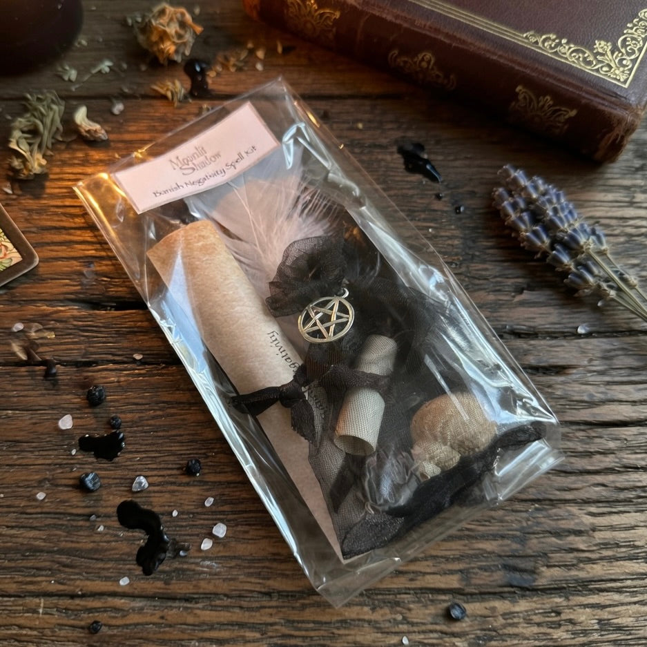 Banish negativity spell kit including a scroll, candle, and black bag on a wooden surface with herb sprinkles and a book