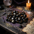 Black onyx rune stones with gold markings on a wooden surface with a candle and lavender.