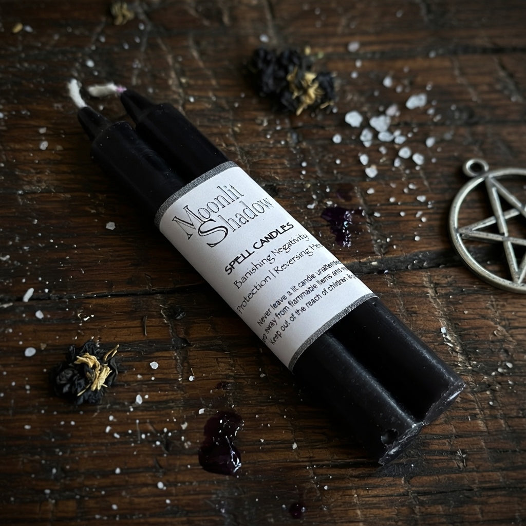 Black spell candle with a label on a wooden surface with dried flowers and a pentagram charm.