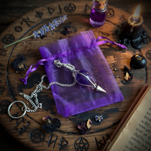 Amethyst pendulum on a purple drawstring pouch with mystical items on an occult carved wooden circle