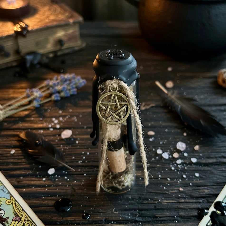 House blessing charm bottle, sealed with wax and a pentagram symbol, containing scroll, herbs, shell, on a wooden surface with a book, lavender and candle in the background