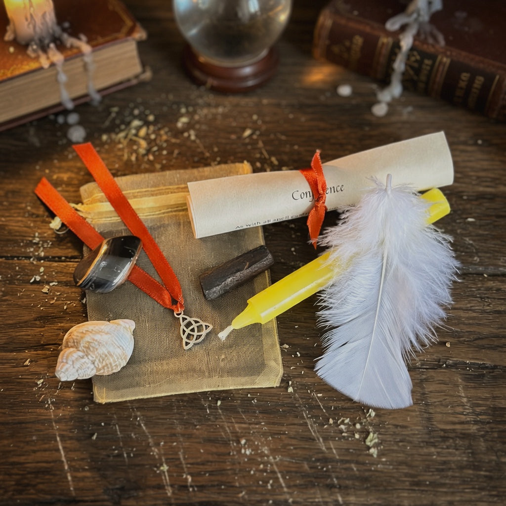 Confidence spell kit with scroll, candle, feather and shell, on a rough wooden surface with books in the background