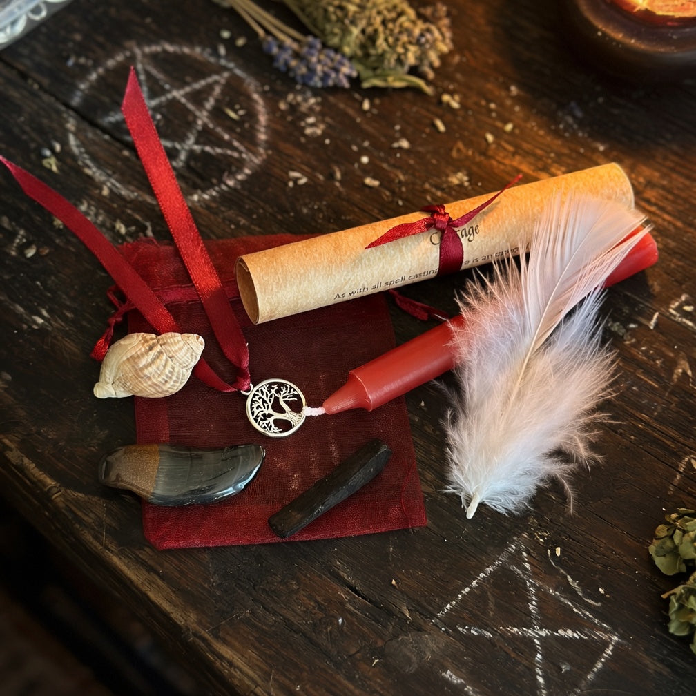 Courage spell kit, with scroll with red ribbon, feather, and candle on a dark wooden surface with occult drawings.