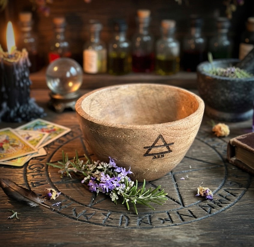 Wooden bowl with herbs on a wooden surface with witchcraft themed mystical items in the background