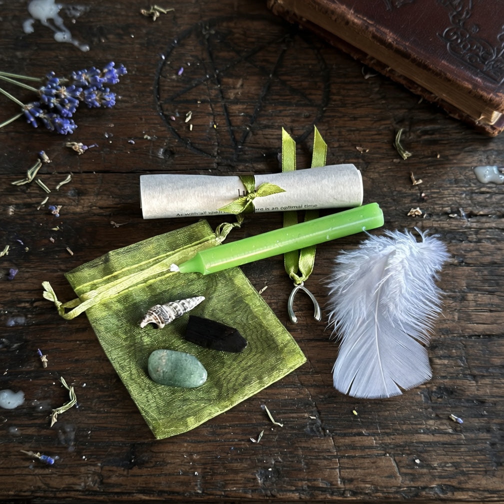 Good luck spell kit with candle, feather, and stone on a wooden surface with occult carvings and lavender flowers.