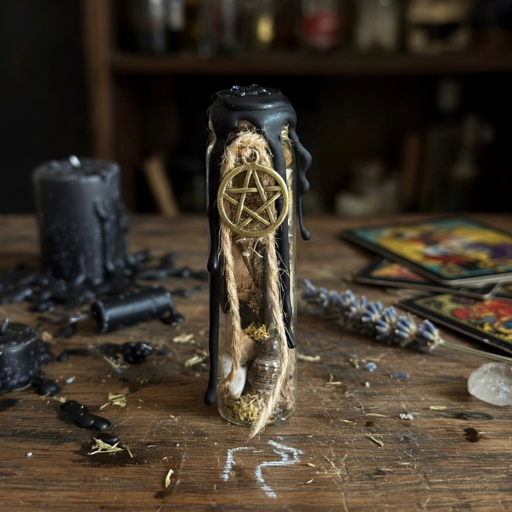 House blessing charm bottle, sealed with black wax and a pentagram symbol, on a wooden surface with tarot cards and a candle in the background