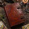 Decorative leather book of shadows with pentagram design on a wooden surface with candles and tarot cards.