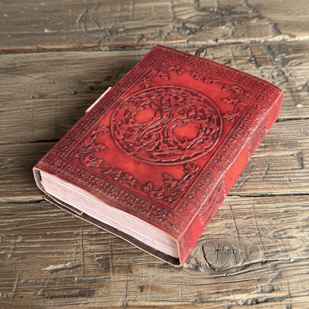 Embossed leather bound tree of life book of shadows, on a wooden surface.