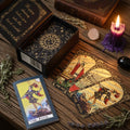 Black with gold foil boxed tarot set, on a wooden surface with candle, herbs and a book