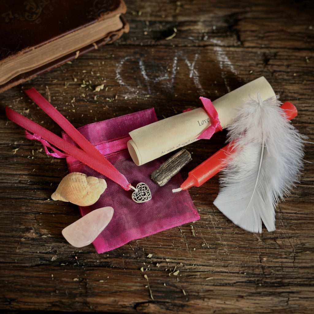 Love spell kit with scroll, candle, feather and shell on rough wooden surface