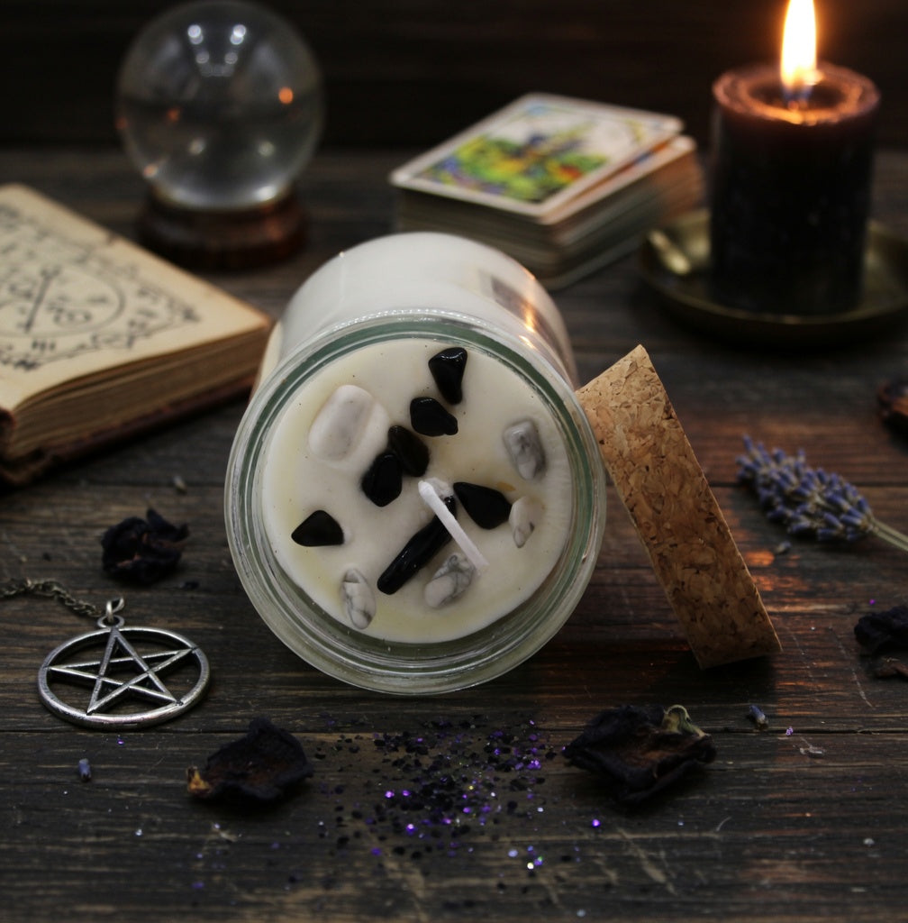 Spell candle in a glass jar with decorative stones on a dark wooden surface with mystical items.