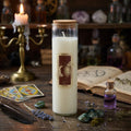 White Friendship spell candle with a label on a wooden table with tarot cards, bottles, and herbs.