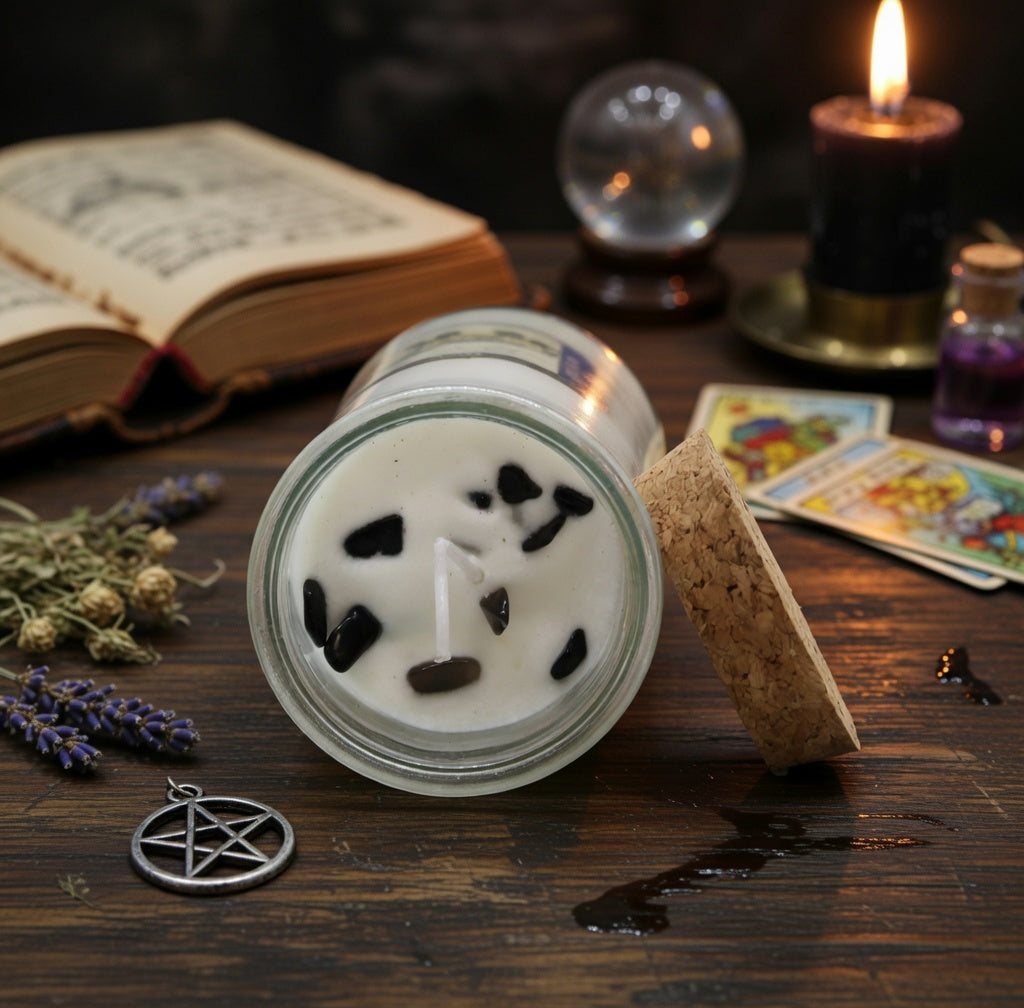Spell candle with black stones on a wooden surface with books, tarot cards, and a crystal ball.