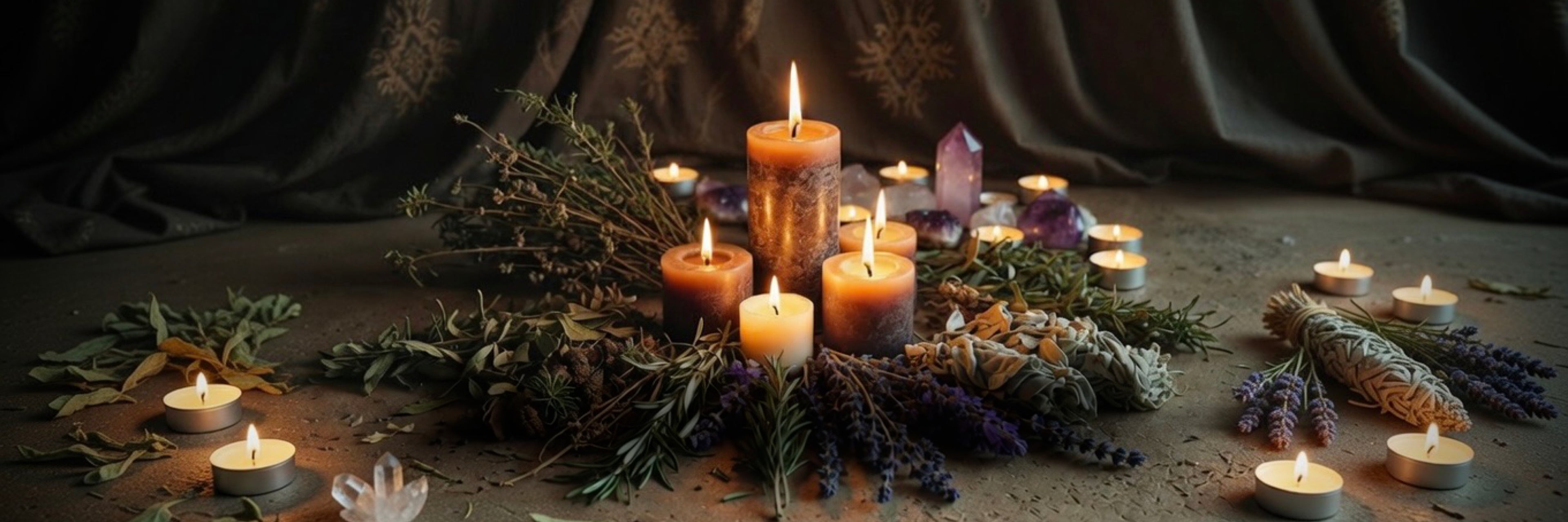 Candles, herbs and crystals arranged on a dark surface with a draped fabric background