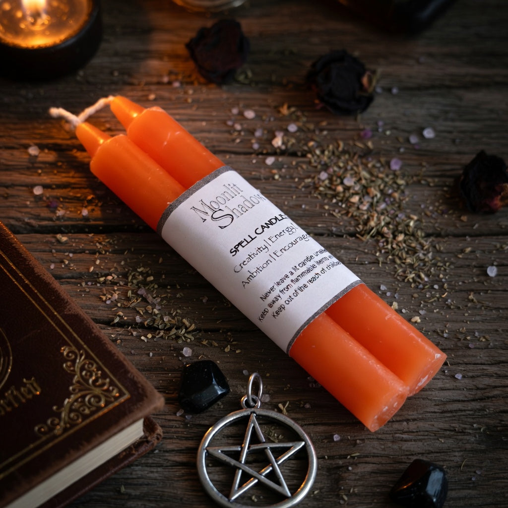 Orange spell candles with a pentagram pendant on a wooden surface.