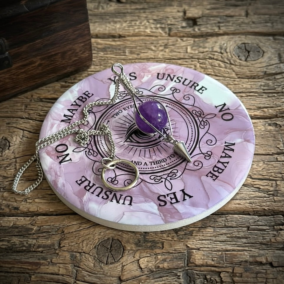Porcelain pendulum divination board and amethyst pendulum, on a rustic wooden surface 
