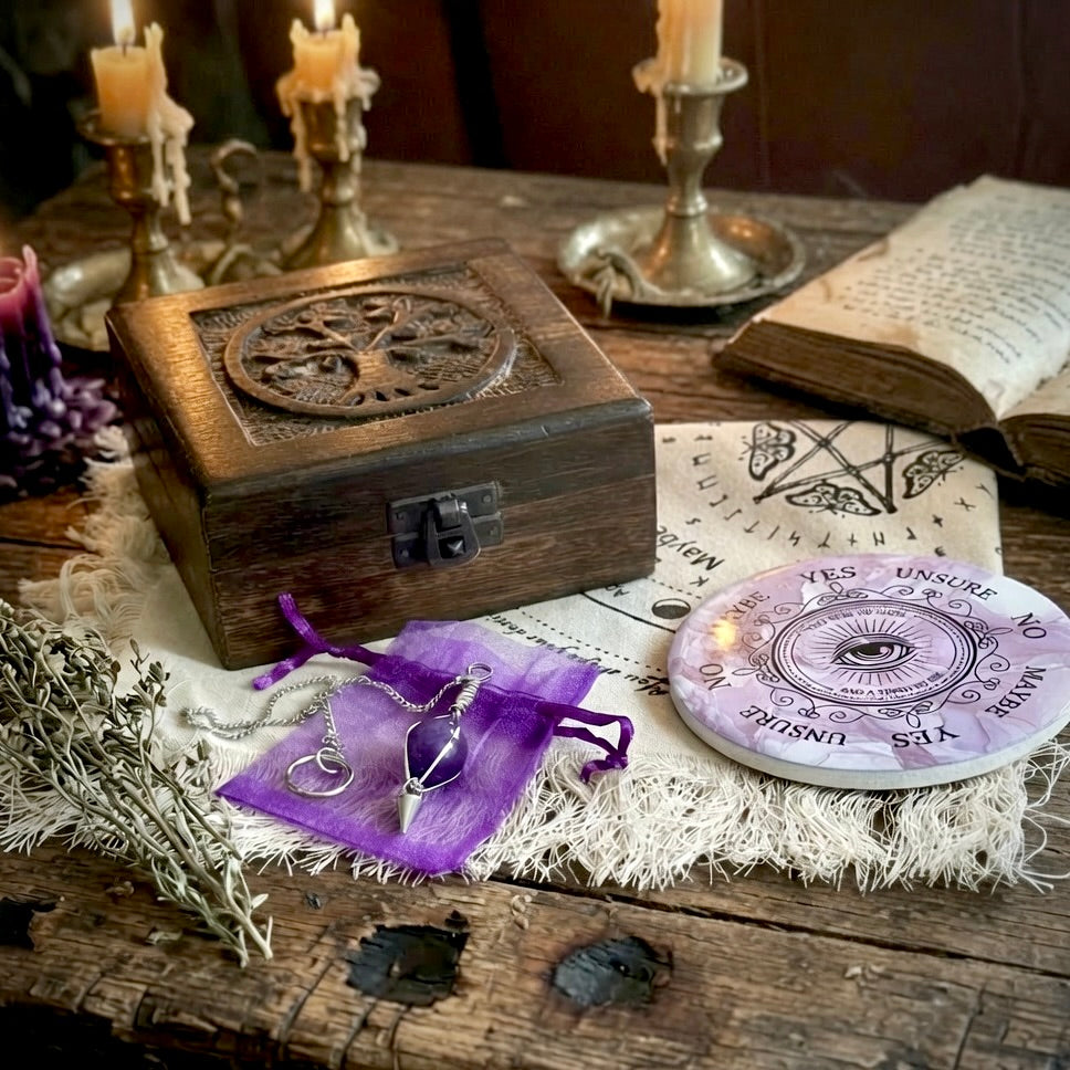 Pendulum divination gift set with cloth, pendulum board, carved wooden box and amethyst pendulum on a rustic wooden table with candles