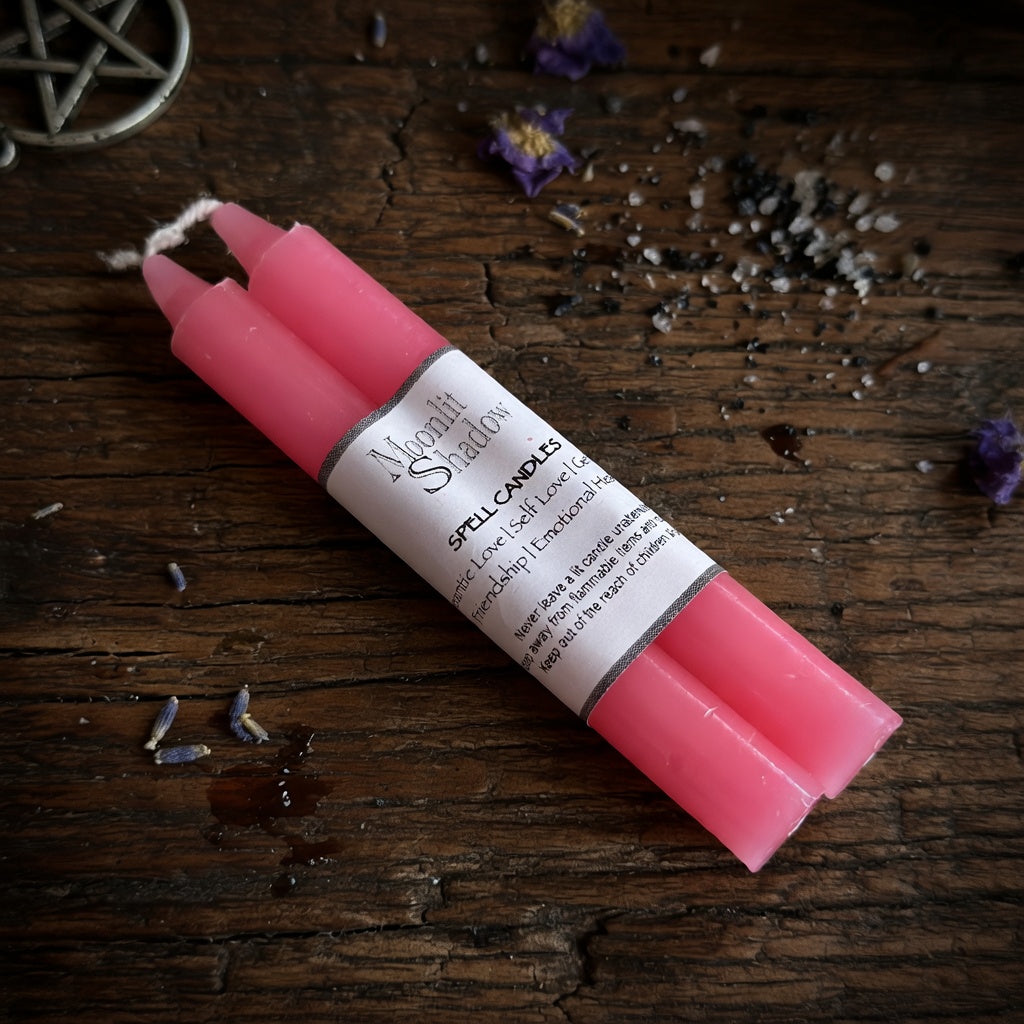 Set of pink spell candles with a label on a wooden surface with dried flowers and herbs.