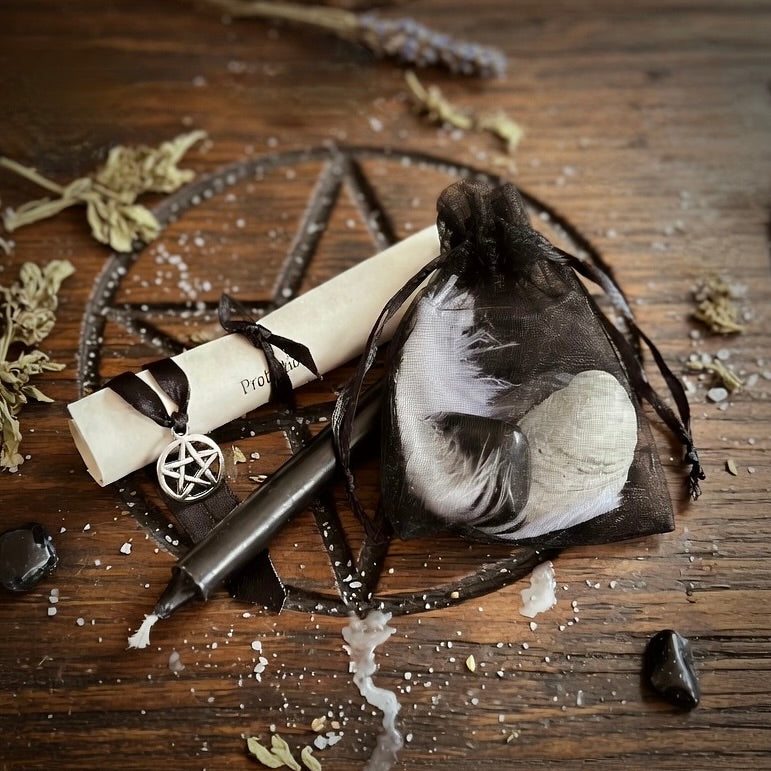 Protection spell kit, including a pentacle charm, feathered and scroll on a wooden surface with occult symbol