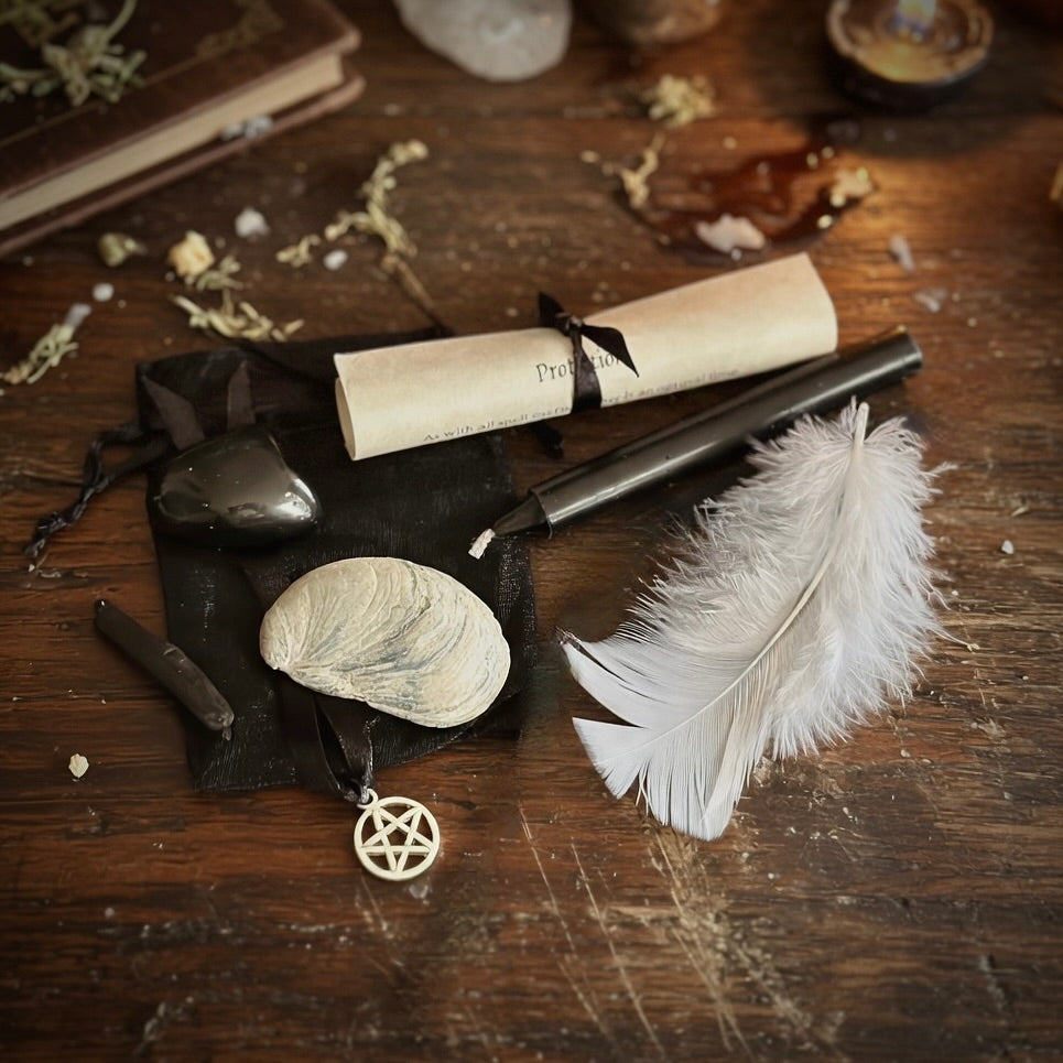 Protection spell kit contents, with scroll, candle, feather and shell, and a dark wood surface