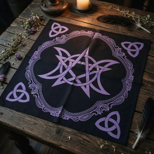 Black altar cloth with purple pentagram and triple moon design, on a wooden surface with candles and herbs.