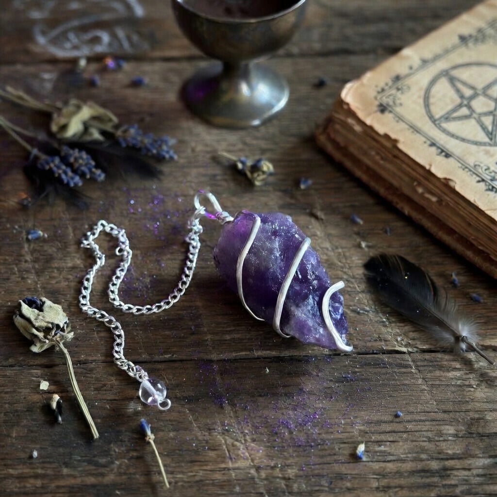 Raw Amethyst crystal pendulum on a wooden surface with dried lavender and a book