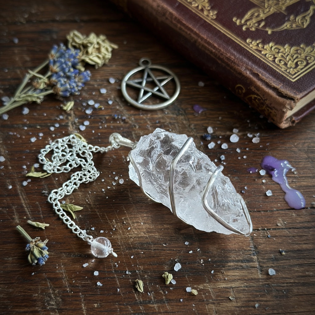 Rock quartz crystal pendulum, and dried flowers on a wooden surface with an old book.
