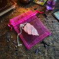 Raw rose quartz pendulum and pink organza pouch on a rough wood surface