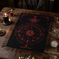 Black pendulum divination cloth with red symbols on a wooden table with candles and cards