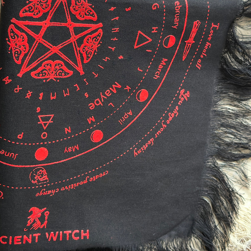Black divination cloth with red witch-themed designs and text, including a pentagram and calendar symbols.