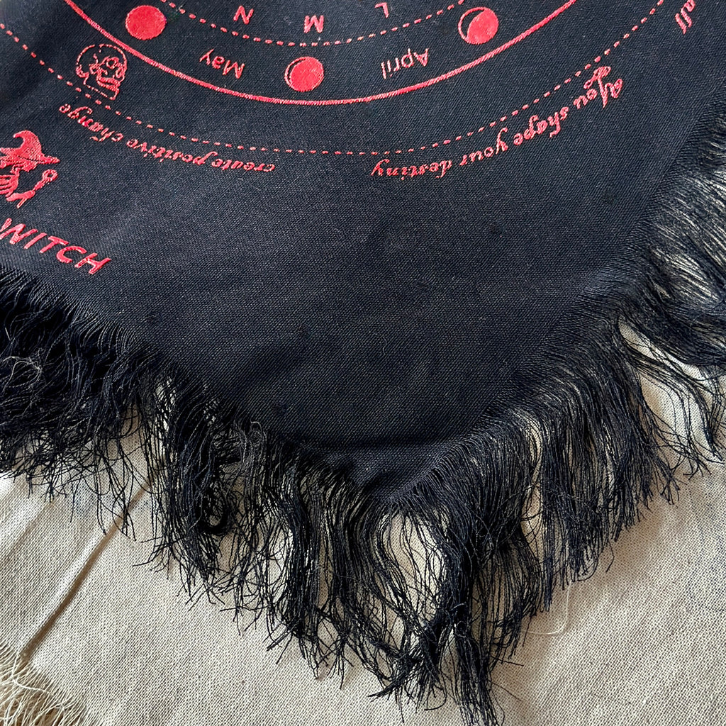 Black divination cloth with red embroidered text and symbols on a beige fabric background