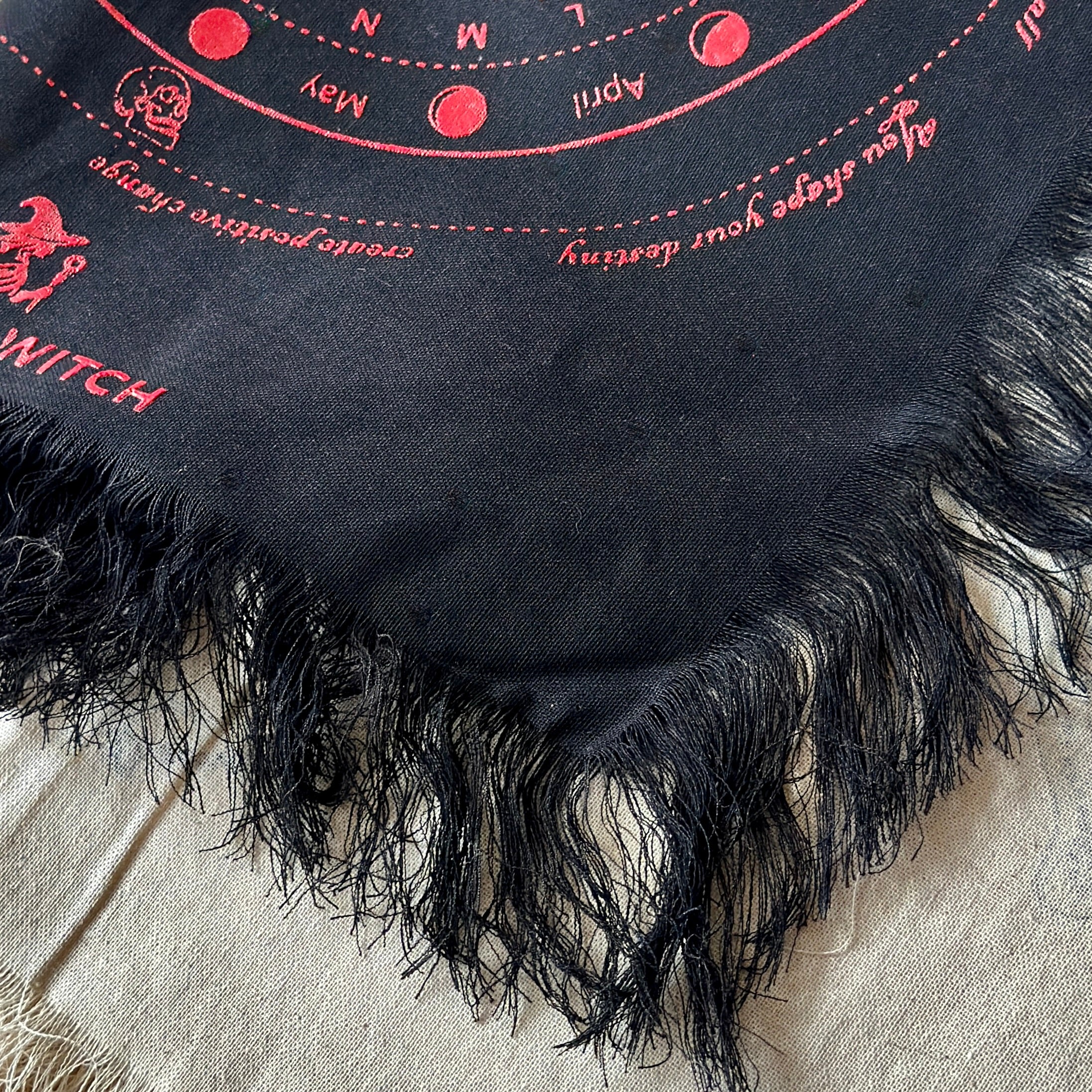 Black divination cloth with red embroidered text and symbols on a beige fabric background