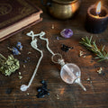 Rock quartz sphere pendulum on a wooden surface with a book and herbs