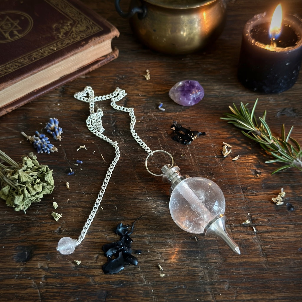 Rock quartz sphere pendulum on a wooden surface with a book and herbs