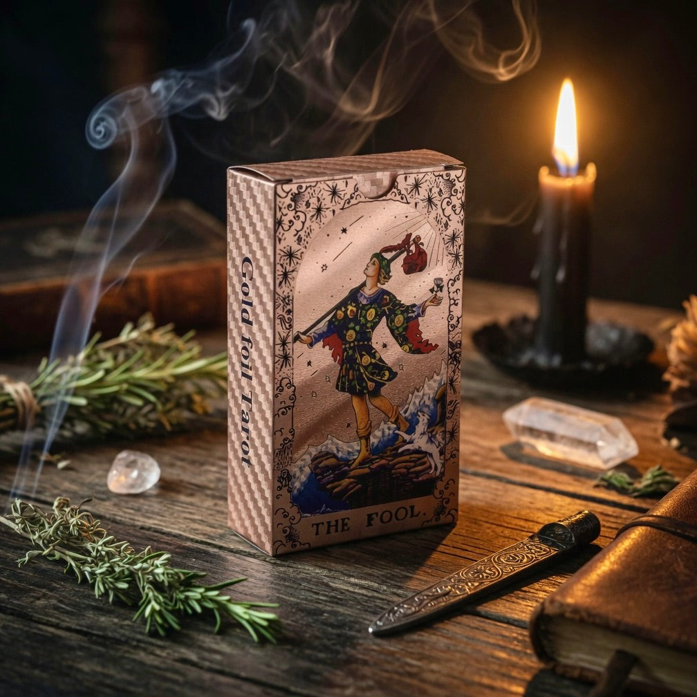 Rose gold  tarot card box featuring 'The Fool' card, surrounded by herbs and a candle on a wooden surface.