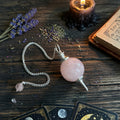 Rose quartz pendulum with chain on a wooden surface with lavender and candles