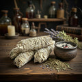 Sage smudge sticks and a bowl on a wooden table with bottles and lavender in the background