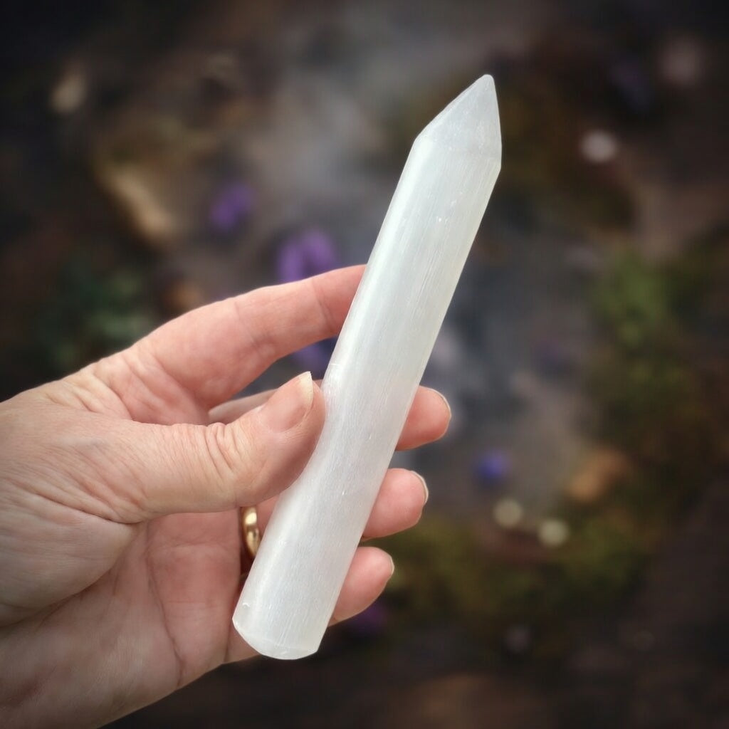 Hand holding a selenite wand against a blurred natural background