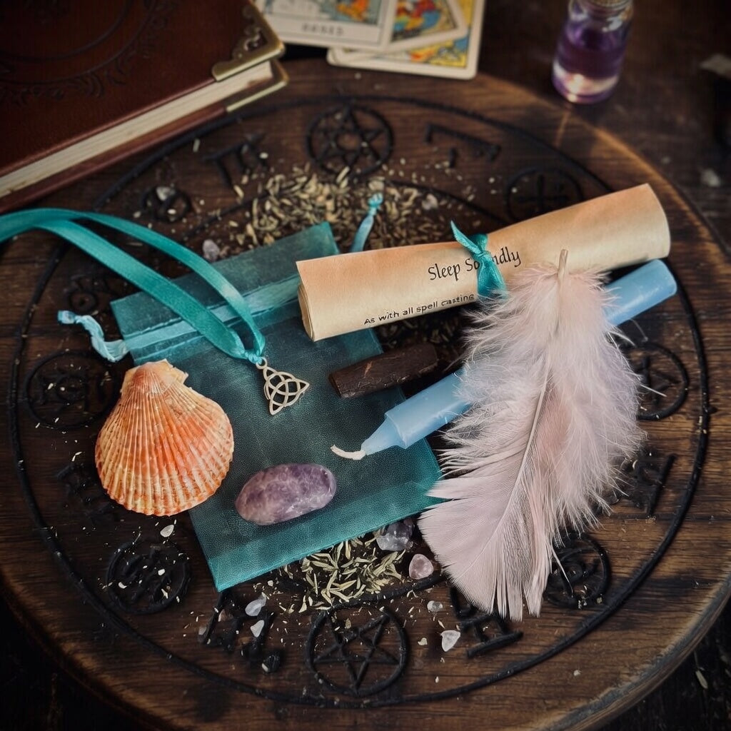 Sleep soundly spell kit, including a feather, shell, and tarot cards on a wooden surface with witchcraft symbols