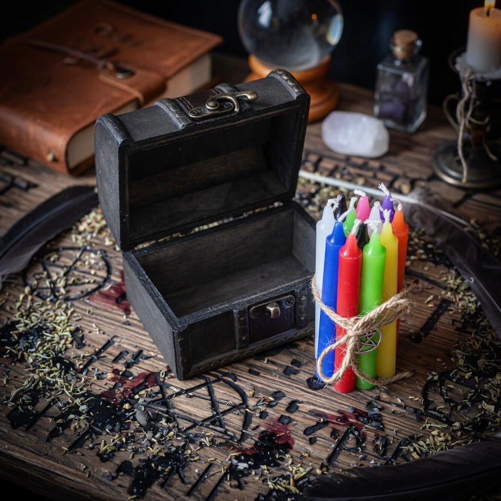 Wooden box with a bundle of twelve coloured spell candles, on a wooden surface with herbs and a lit candle