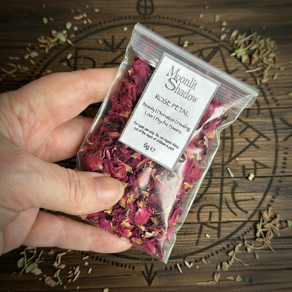Hand holding a package of rose petals labeled 'Moonlit Shadow' on a wooden background.