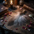 Spotted smudging feathers on a wooden surface with candles and books, evoking a mystical or magical atmosphere.