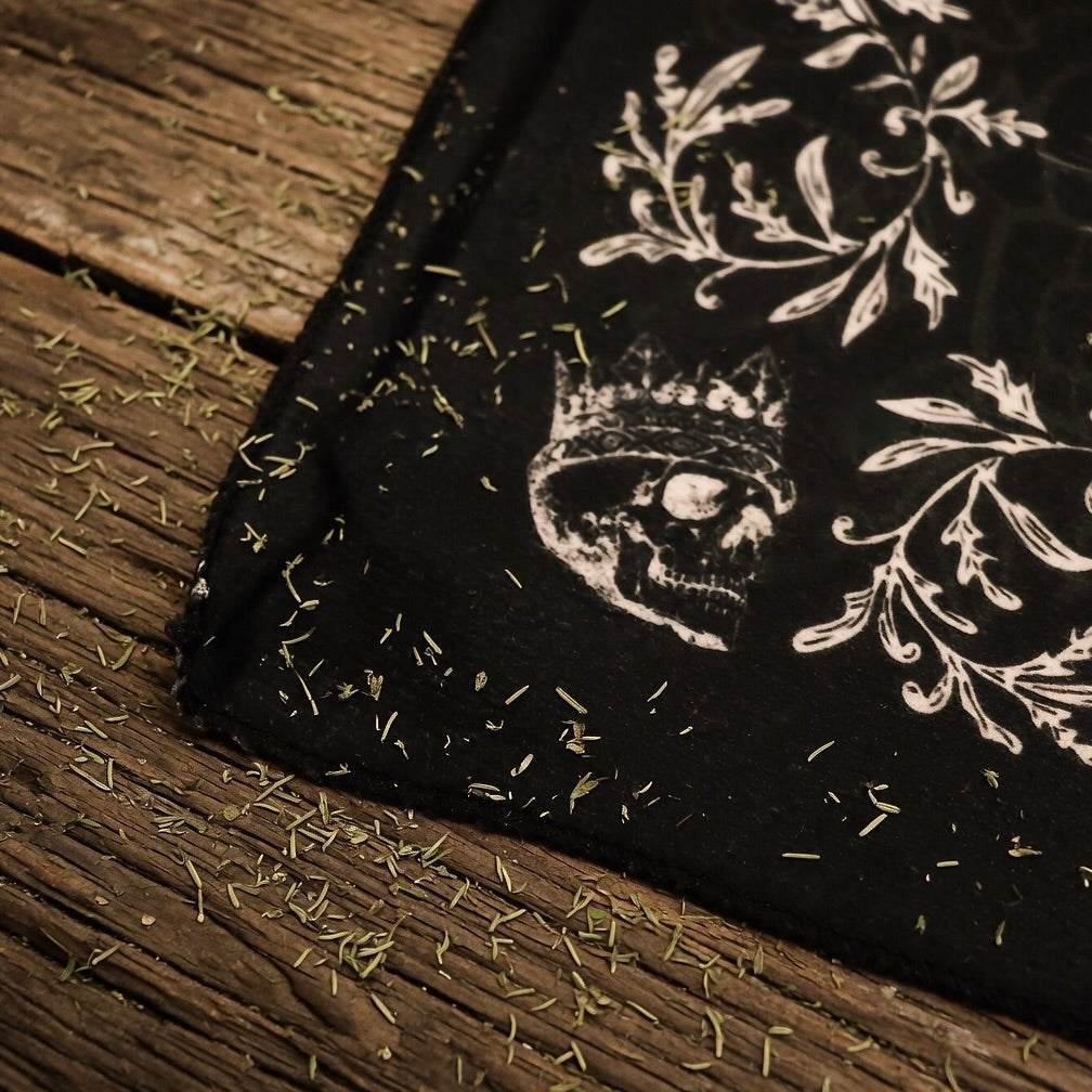 corner of a black tarot reading cloth, with herb sprinkles on wooden surface