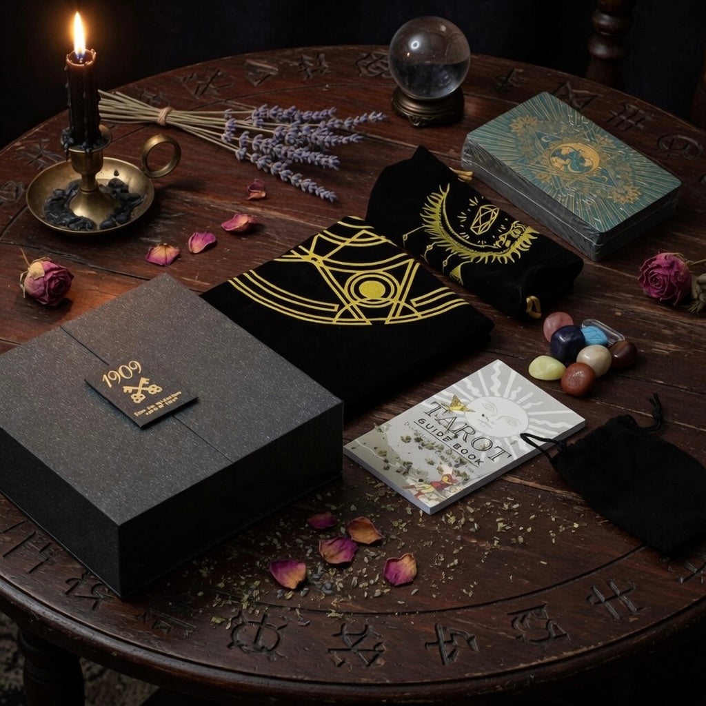 Teal and gold tarot gift set including presentation box, tarot cloth, cards, and tarot guide book, on a carved wooden table with herbs